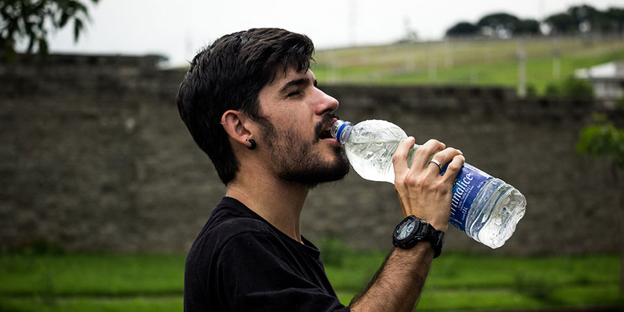 man with short black hair and short trimmed beared wearing a black tshirt drinking water from a bottle